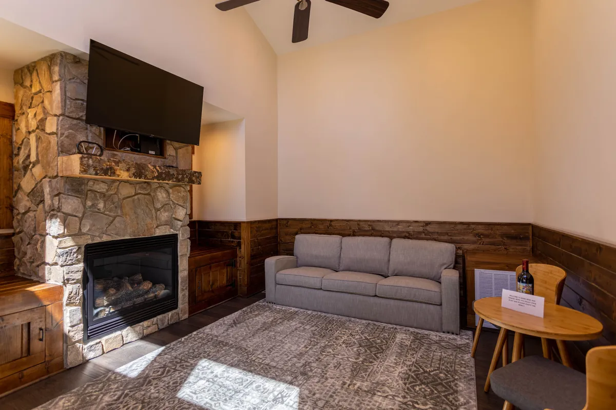 This image showcases a stone fireplace as the focal point, surrounded by a plush, inviting sofa and rustic wooden accents. A coffee table sits in front of the seating area, creating a space ideal for relaxing, socializing, or enjoying movie nights. The soft lighting and natural textures evoke warmth and comfort.