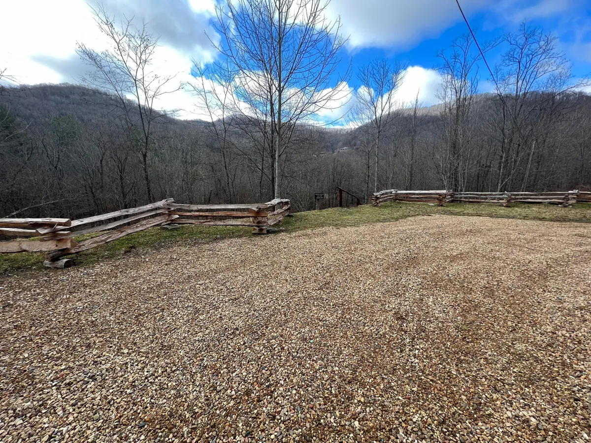 This image features a tranquil exterior scene with a gravel driveway bordered by a wooden fence, distant rolling hills, and bare trees, all bathed in soft natural light. The open space and unobstructed views evoke a sense of freedom and connection to the outdoors, ideal for pet-friendly activities such as walking and exploring with dogs.