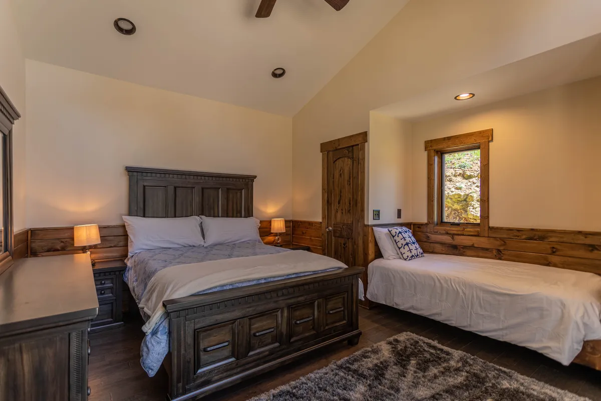 An inviting bedroom scene featuring a king-sized bed, a softly lit nightstand, and a window streaming in natural light. The wooden door hints at the home’s cozy, welcoming atmosphere. While primarily an interior, the visible natural light and restful mood subtly underscore the idea of a relaxing home base after outdoor adventures with pets.