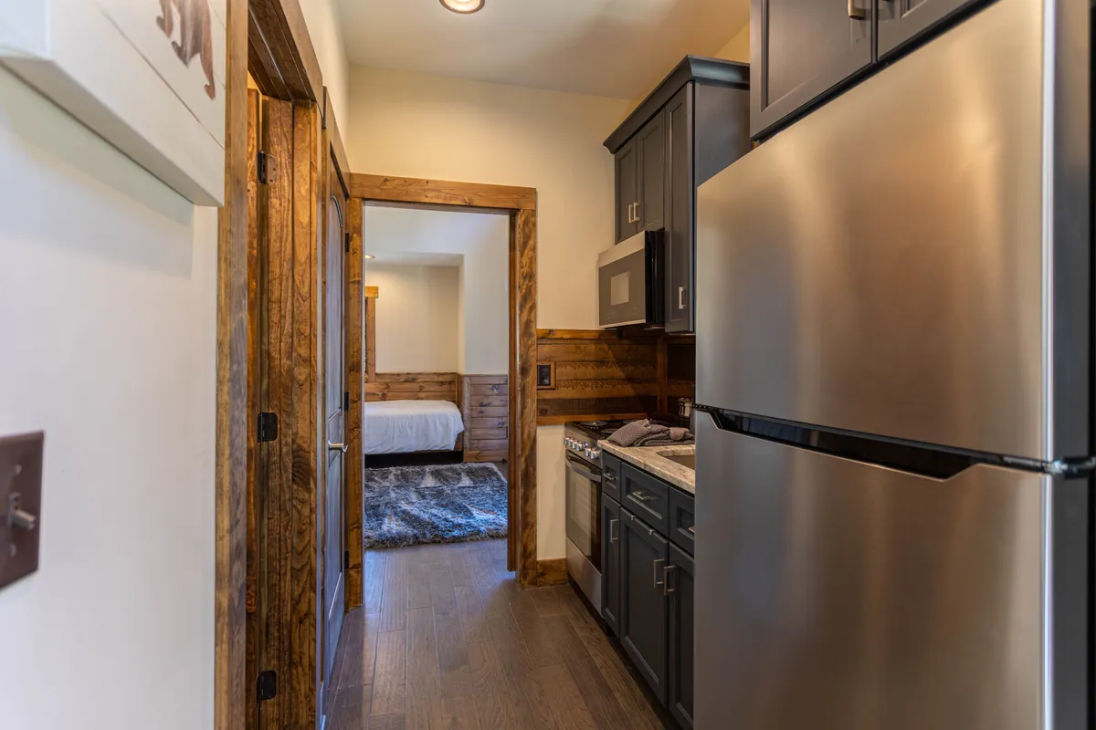 A warm, inviting kitchen scene featuring modern stainless steel appliances and wooden cabinetry. The open layout provides a glimpse into an adjoining room, suggesting easy flow for both cooking and entertaining. The kitchen appears ready for gourmet meal prep or casual dining, with ample counter space and a cozy, welcoming ambiance.