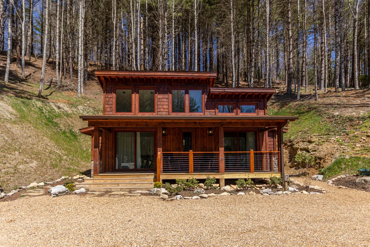 An exterior view of a welcoming wooden cabin with a spacious front porch, large windows, and an inviting facade. The porch suggests a perfect spot for outdoor gatherings, barbecues, or watching the sunset, surrounded by natural beauty.