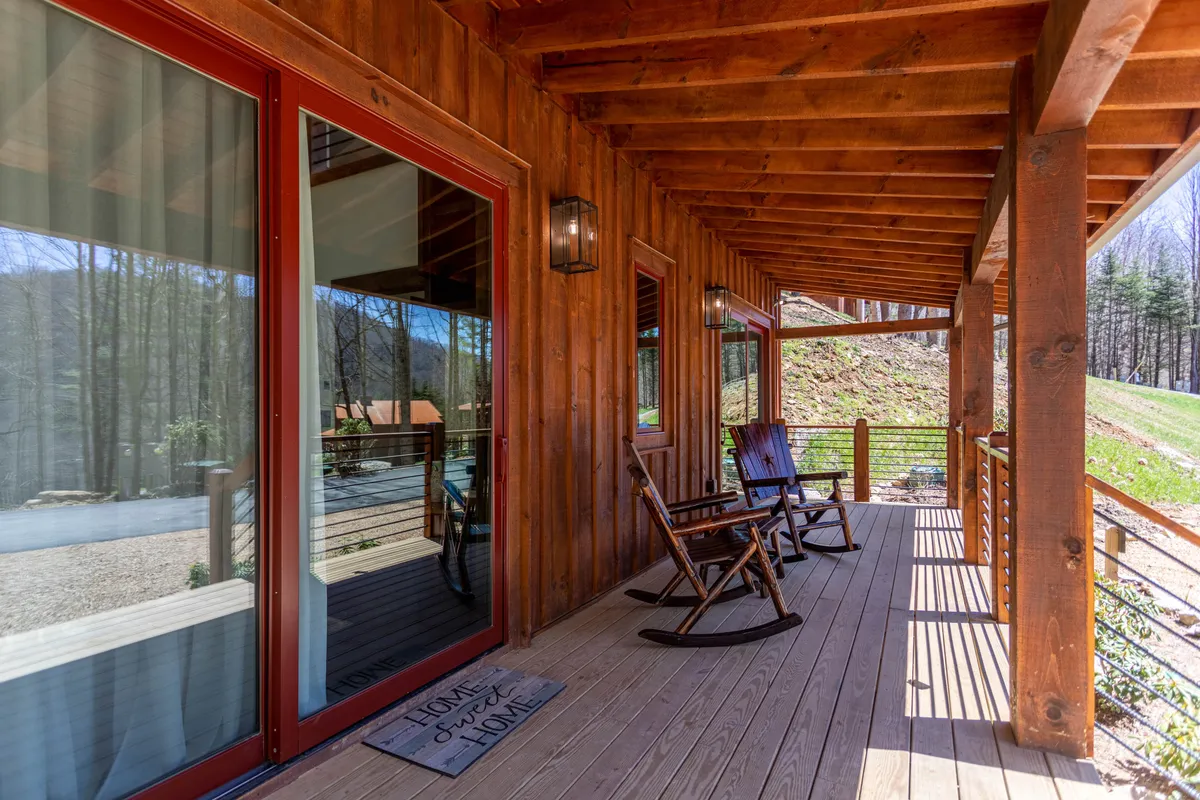 This exterior image showcases a cabin's wooden porch with inviting rocking chairs and large glass windows that open to nature views. The seating area is perfect for relaxing, reading, and enjoying the serene mountain surroundings, hinting at the indoor-outdoor living experience described in the section.