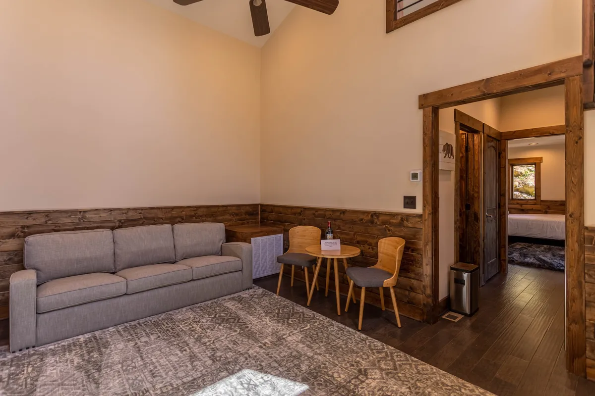 A warm and inviting living space is showcased with a comfortable sofa, a nearby dining table, wood paneling, and a statement light fixture. The intimate setting is perfect for relaxing, socializing, or reading, with the suggestion of a homey and welcoming atmosphere.